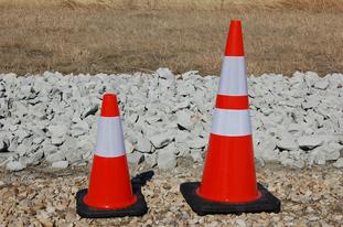 Two traffic cones on rocky ground.